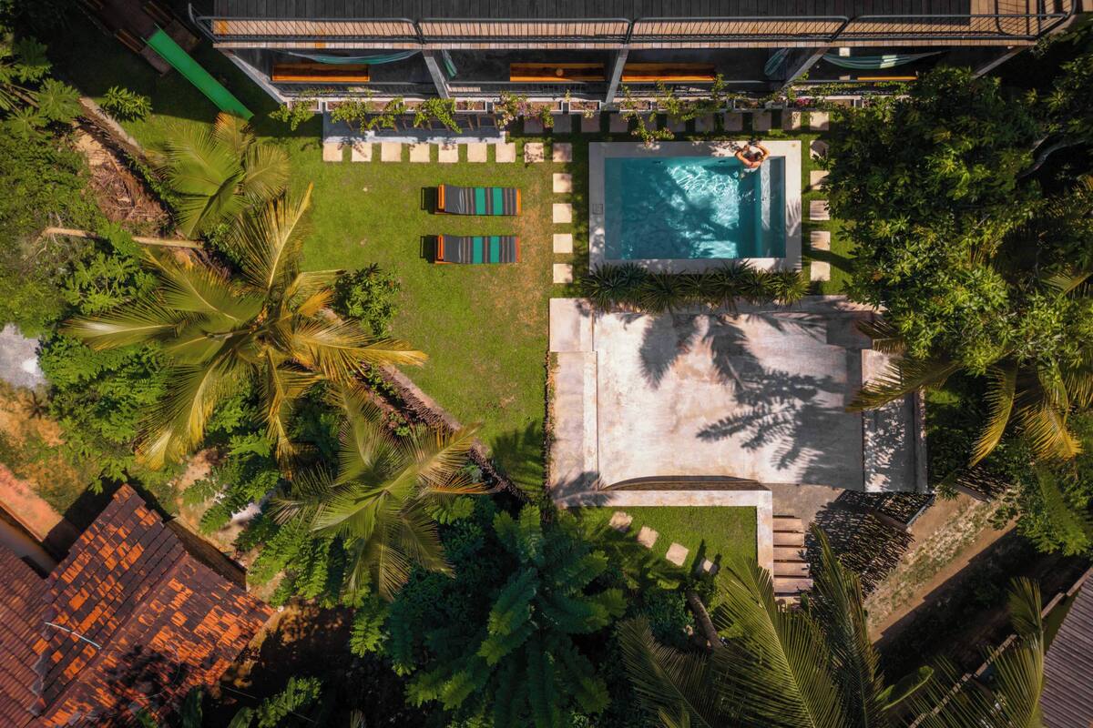 An aerial view of a resort with a swimming pool, lounge chairs, and lush greenery.
