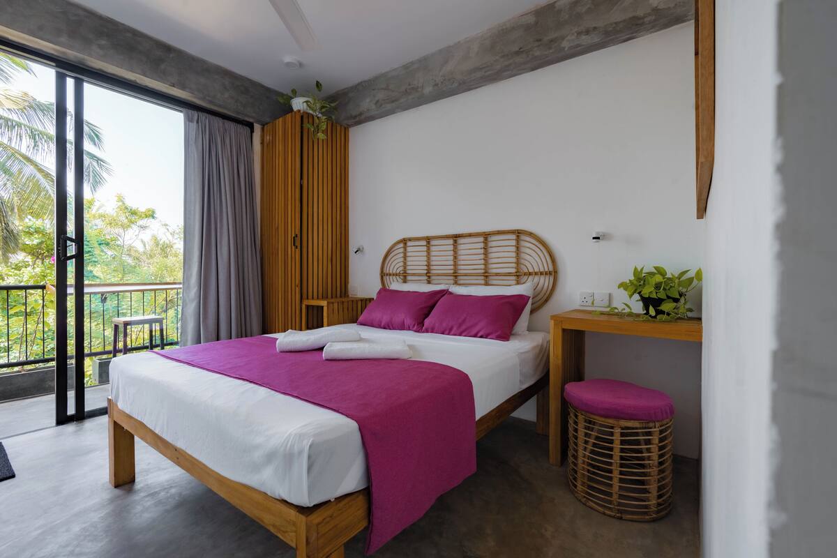 A modern bedroom with a wooden bed, a balcony, and a view of greenery.
