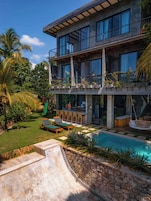 A modern two-story house with a pool, outdoor seating, and lush greenery.
