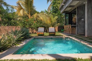 A rectangular pool with two lounge chairs facing it, surrounded by lush greenery and a wooden fence. - Gaia Soul  (Maaliyadda)