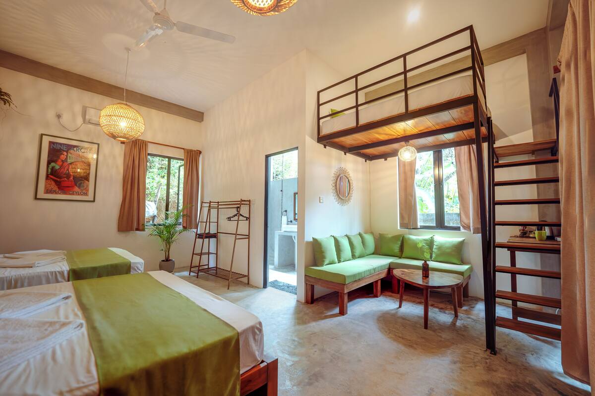 A room with bunk beds, a sofa, a ladder, and a hanging light fixture.