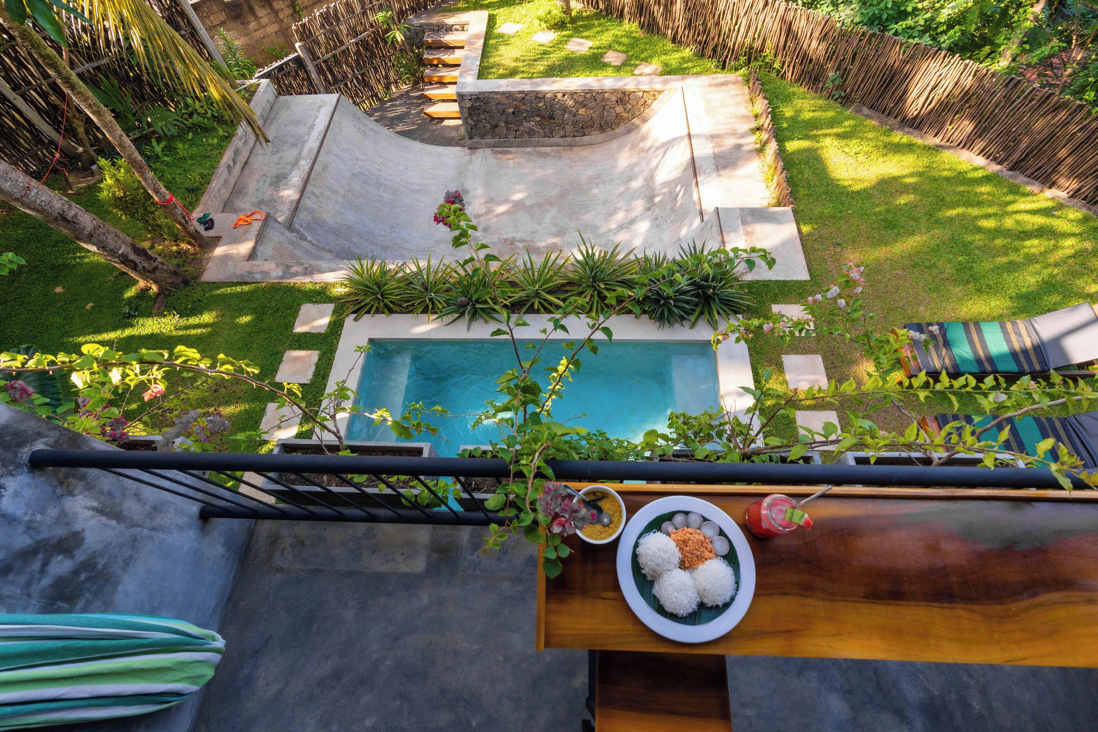 A rooftop pool with a stone border, surrounded by lush greenery and a wooden deck.