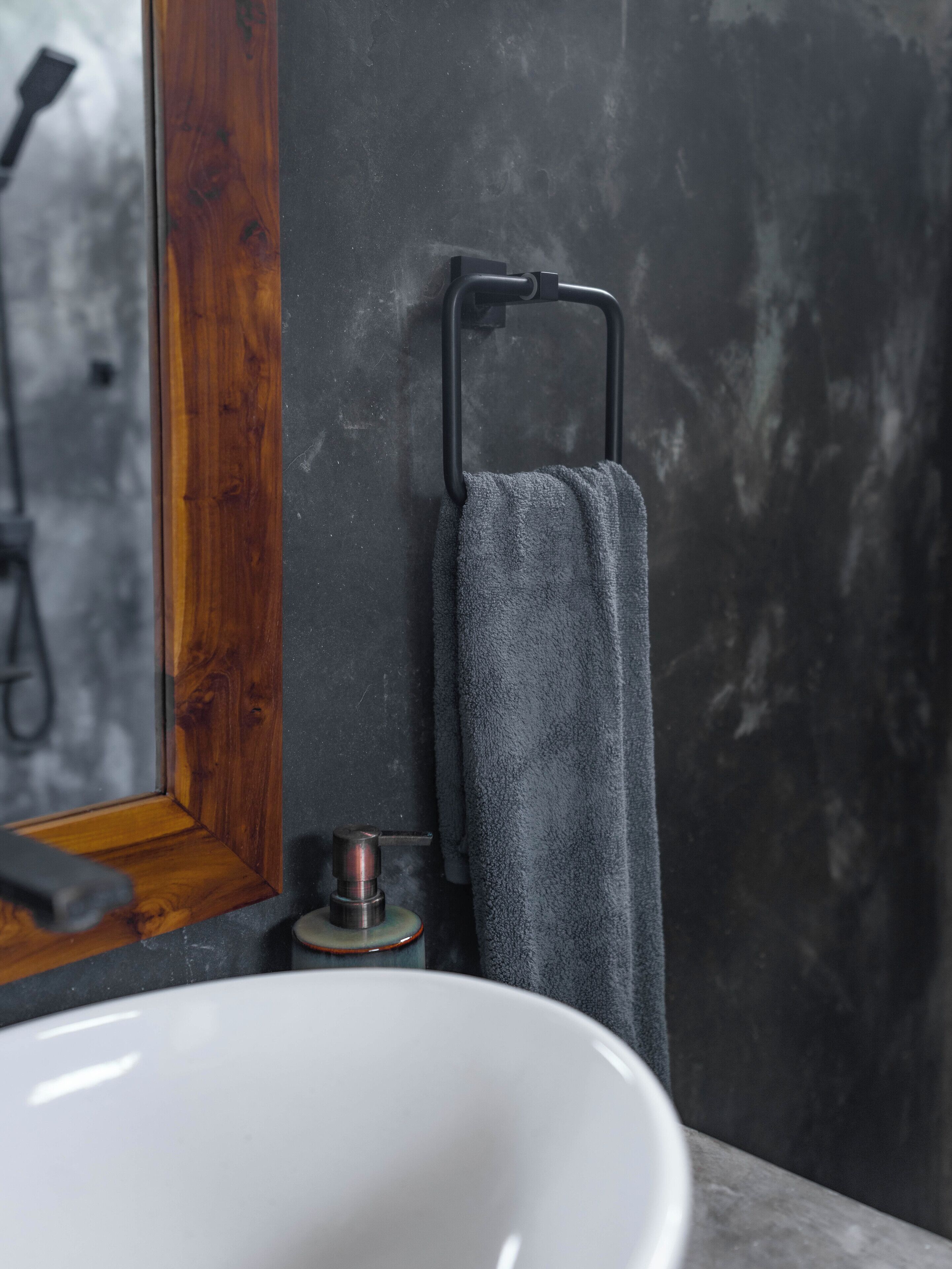 Ein Badezimmer mit einem weißen Waschbecken, einem spiegel mit Holzrahmen und einem Handtuch an einem schwarzen Handtuchhalter.