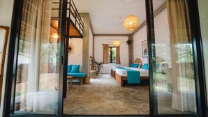 A spacious room with a large sliding glass door leading to an outdoor area. The room has a bed with blue bedding, a sofa, and a small table. There is a ceiling fan and a hanging light fixture. - Gaia Soul  (Maaliyadda)