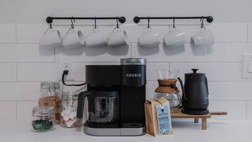 Une cuisine équipée d’une machine à café Keurig, de capsules de café, d’une bouilloire et d’un moulin à café.