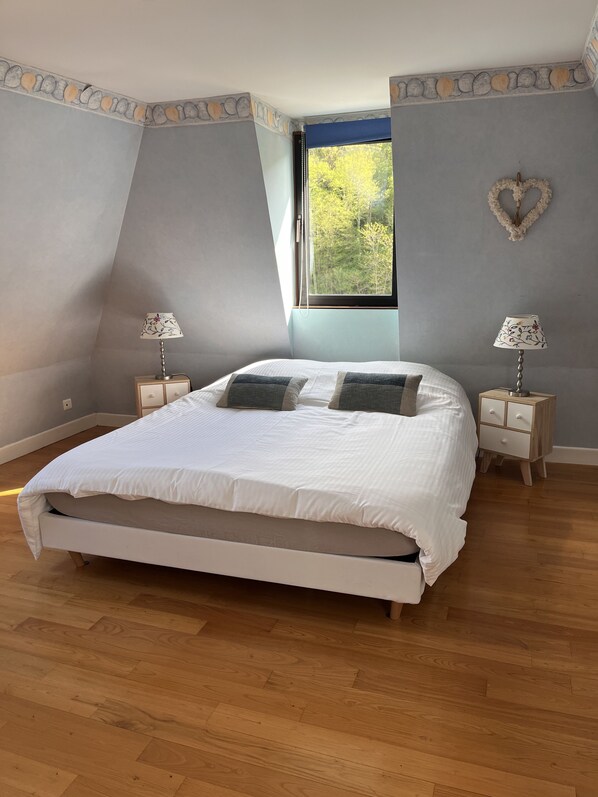 Un dormitorio con una cama grande, dos mesitas de noche, una ventana con vista a árboles y un borde decorativo en la pared.