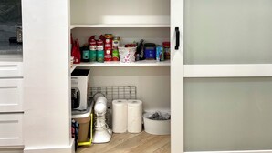 A kitchen with a sliding door pantry containing food items, a kettle, and a mixer.