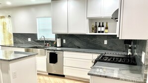 A modern kitchen with white cabinetry, a marble countertop, and a built-in gas stove.