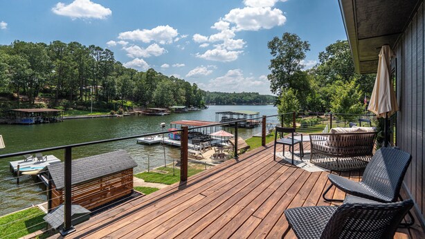 Una terraza de madera con mobiliario exterior con vistas a un lago, muelles y barcos.