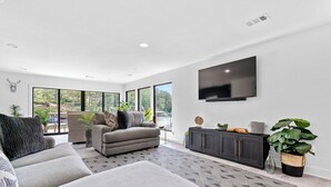 Una sala de estar moderna con un sofá gris, un sillón gris, un mueble de entretenimiento negro y un televisor grande en la pared.