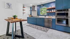 Una cocina moderna con armarios azules, electrodomésticos de acero inoxidable y una mesa de madera con una pizza.