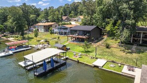 Una propiedad frente al lago con muelle, mobiliario exterior y una casa grande con terraza.