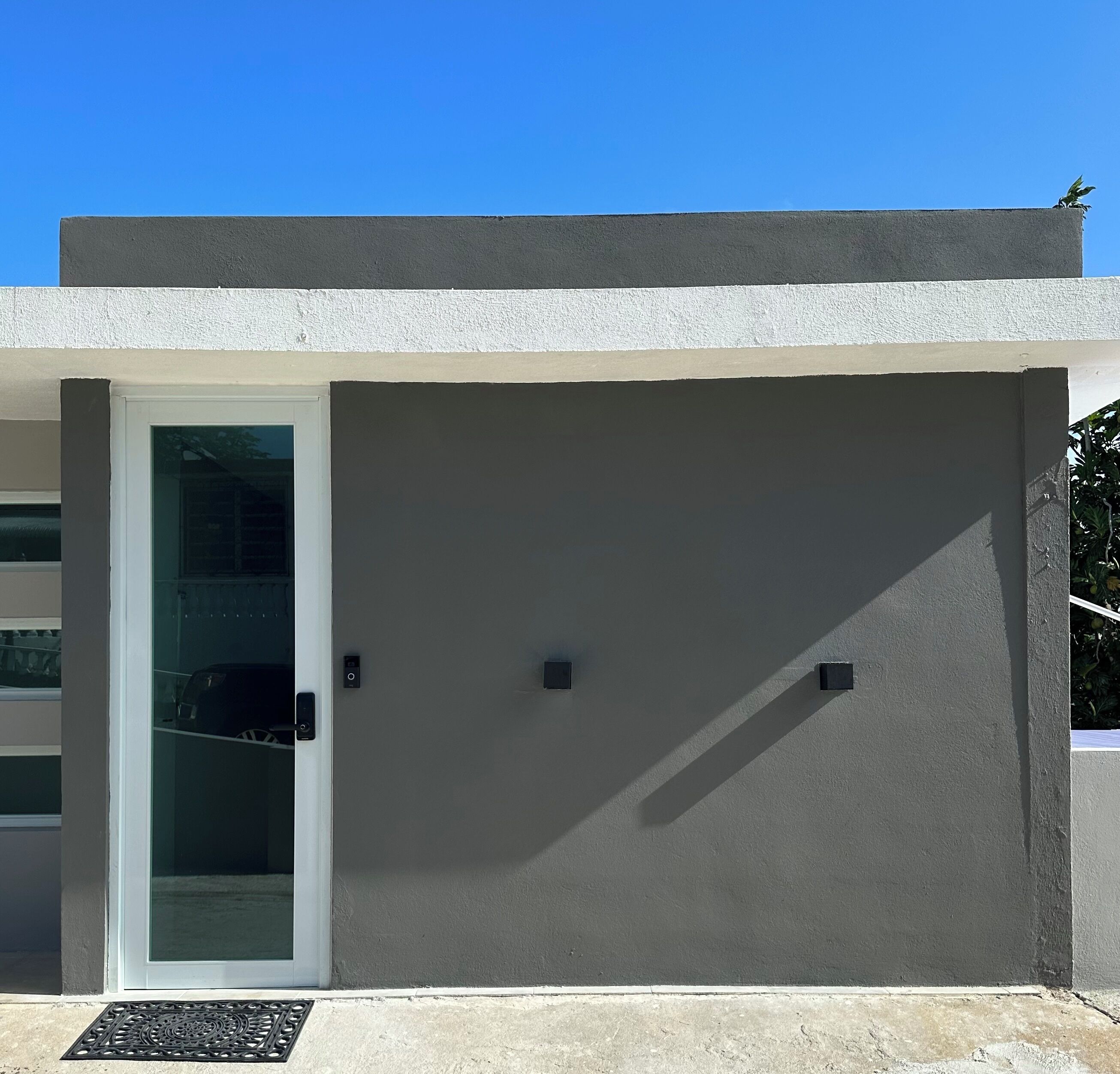 Fachada de edificio moderna con puerta de vidrio, una ventana pequeña y un respiradero de metal.