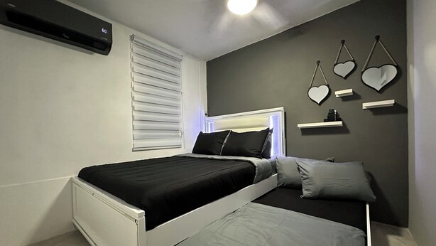 A bedroom with a bed, bedside tables, a wall-mounted heater, and heart-shaped decorations. - Shely’s Apartment#2 (Ceiba)