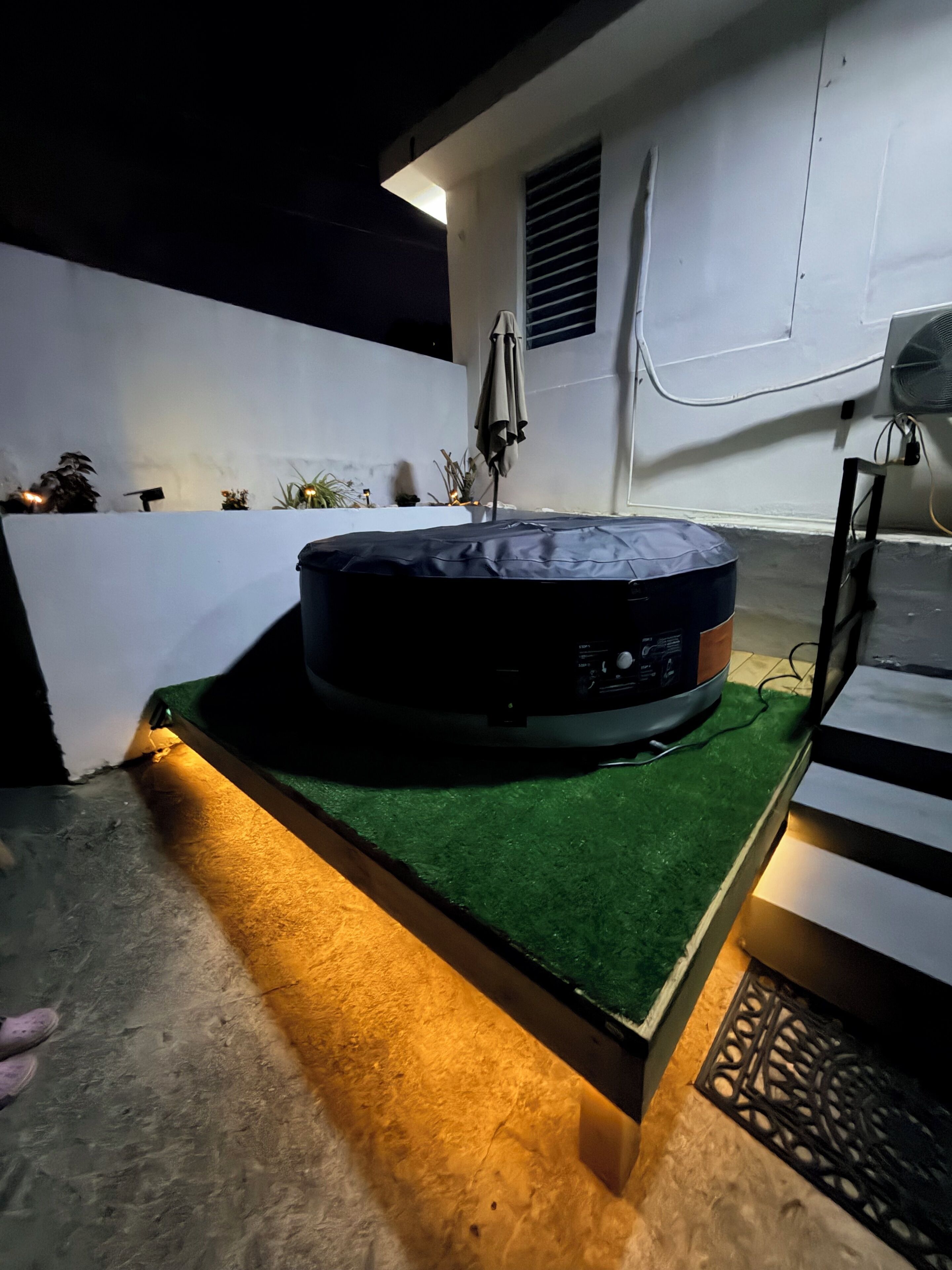A room with a circular object on a green platform, a white wall, and a window with blinds.