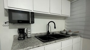 A kitchen with white cabinets, a black microwave, a coffee maker, and a sink. - Shely’s Apartment#2 (Ceiba)