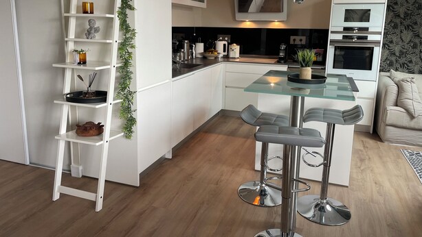 Et moderne køkken med hvide skabe, en glasø med barstole og en hængende lampe.