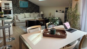 En moderne stue med spiseplads, en sofa, et sofabord, en bærbar computer og en potteplante.
