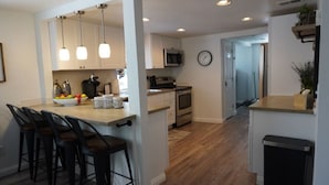 A modern kitchen with a central island, bar stools, a microwave, and a clock on the wall. - Whole House in N. Denver with hot-tub (Denver)