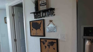 A wall with a 'WELCOME' sign, a framed map of the USA, a framed world map, a sign asking guests to place a map on the wall, and a 'knoxcourt' sign with a bicycle and 'WIFI Password' label. - Whole House in N. Denver with hot-tub (Denver)