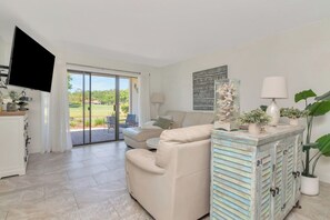 A living room with a sofa, a television, a cabinet, and a view of the outdoors. - Renovated Saddlebrook 1st Floor Condo 2bd/2ba (Wesley Chapel)
