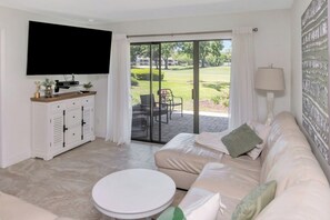 Een moderne woonkamer met een bank, een flatscreen televisie, een salontafel en een schuifdeur naar een buitenruimte.