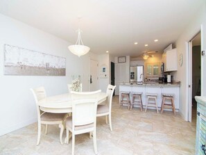 Un'area pranzo con un tavolo e sedie bianche, un lampadario e una cucina sullo sfondo.
