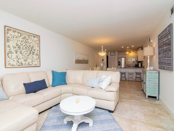 Un salon avec un canapé d’angle beige, une table basse ronde et un tapis bleu.