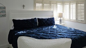 Une chambre à coucher avec un lit, une tête de lit blanche et une fenêtre avec des volets.