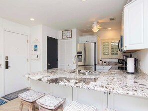 A kitchen with a granite countertop, stainless steel appliances, and a bar stool. - Renovated Saddlebrook 1st Floor Condo 2bd/2ba (Wesley Chapel)