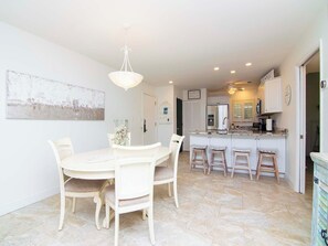 Une cuisine moderne avec des meubles blancs, un îlot central doté de tabourets et un coin repas comprenant une table ronde et des chaises.