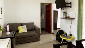 A living room with a sofa, a TV mounted on the wall, a fan, and a small table with a plant.