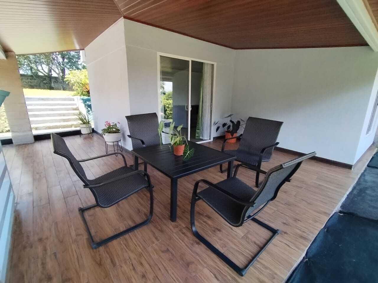 Un patio cubierto con una mesa, cuatro sillas, una planta en maceta y una puerta corrediza de vidrio que da a un espacio exterior.
