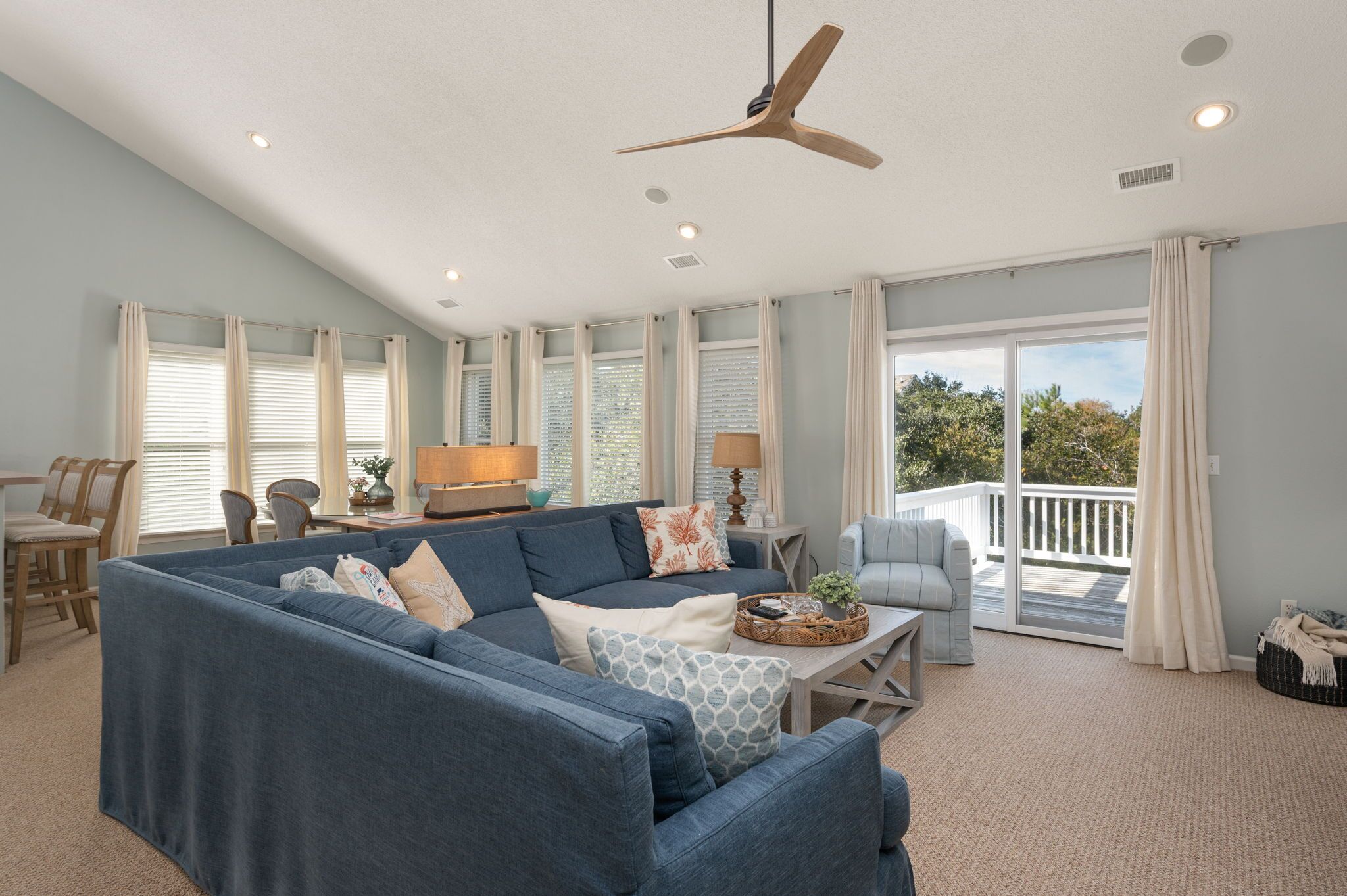 A spacious living room with a large blue sectional sofa, a ceiling fan, and a view to the outside.