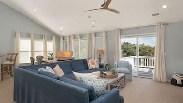 A spacious living room with a large blue sectional sofa, a ceiling fan, and a view to the outside.