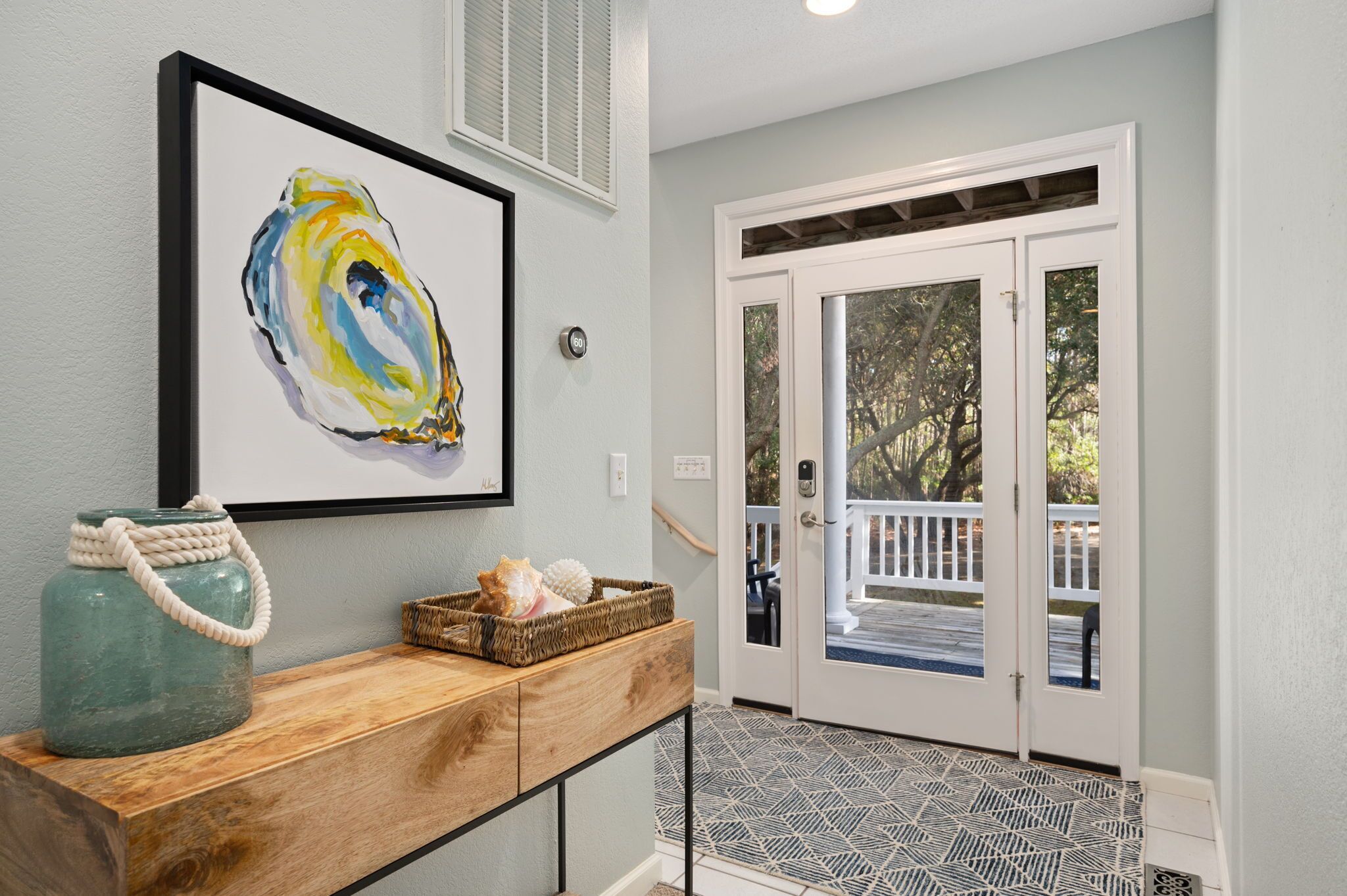 A hallway with a wooden console table, a framed abstract painting, a basket with a rope handle, and a door leading to an outdoor area with a railing.