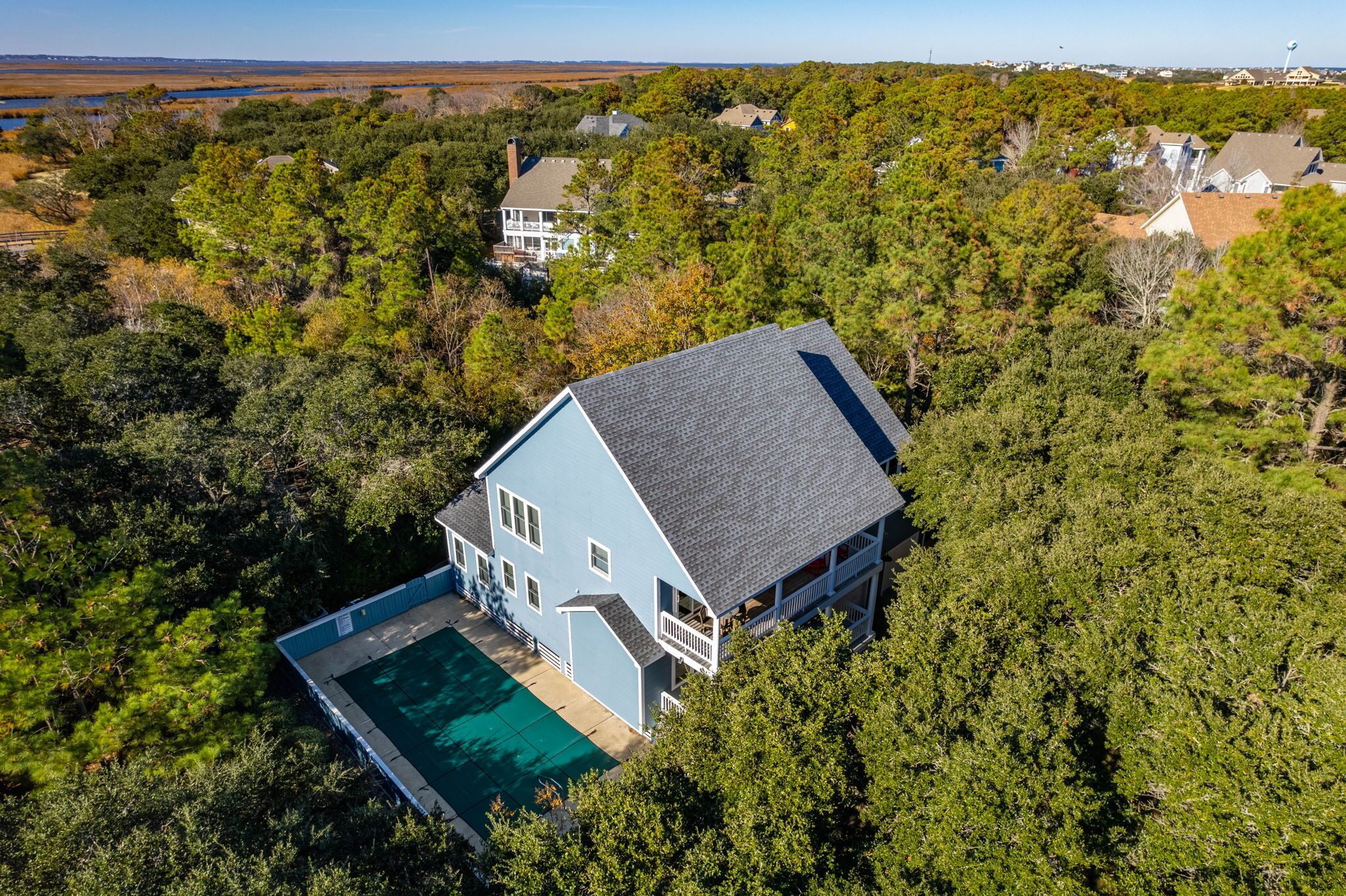 An aerial view of a house with a swimming pool surrounded by dense trees.