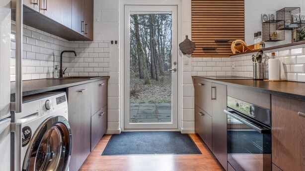 A compact kitchen with a washing machine, oven, and wooden cabinets.