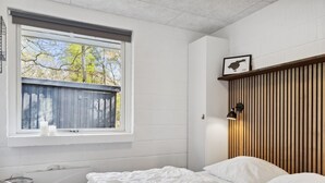 A bedroom with a large window, a wooden slat wall, and a bed with white bedding.