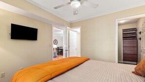 Ein Schlafzimmer mit Bett, Deckenventilator, Wand-Fernseher und begehbarem Kleiderschrank.