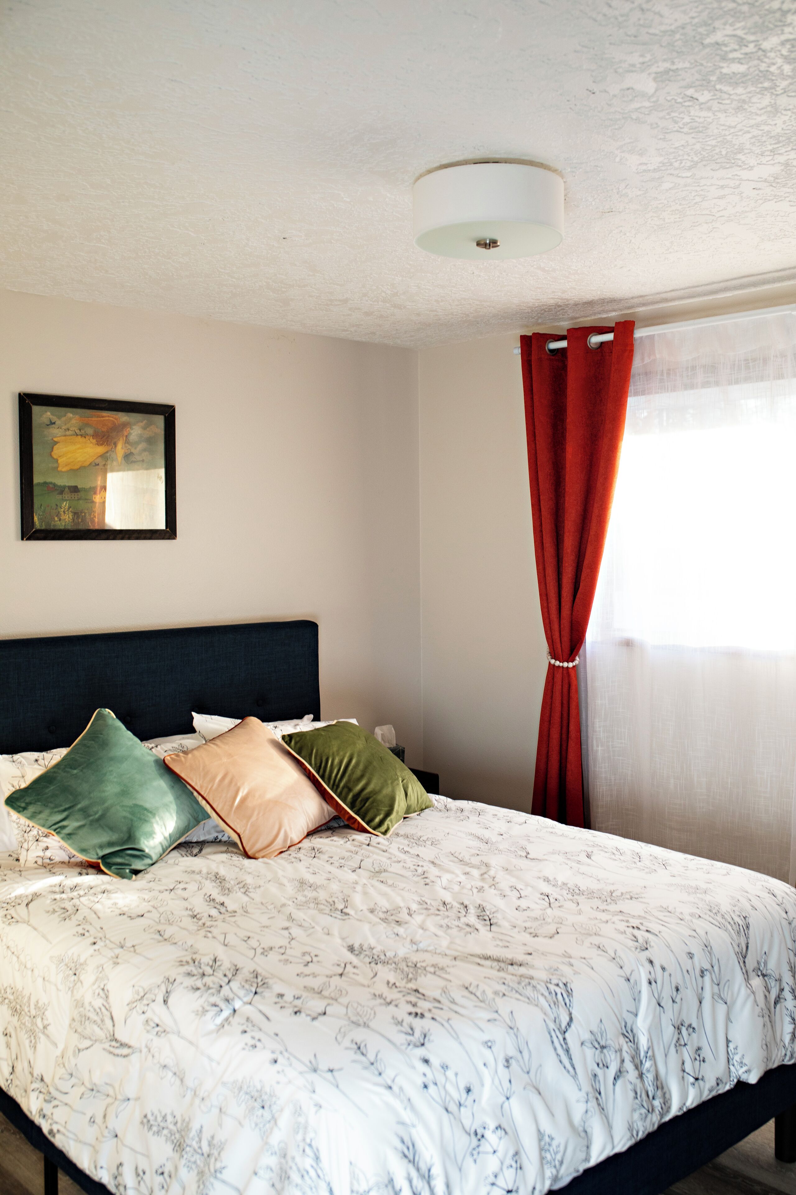 A neatly made bed with a floral-patterned bedspread, a dark headboard, and a framed picture on the wall.