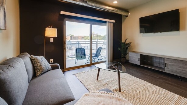 A modern living room with a sofa, a glass coffee table, and a TV mounted on the wall. - Cozy 1B1B w/Wi-Fi, Balcony Views, Coffee + Parking (Des Moines)