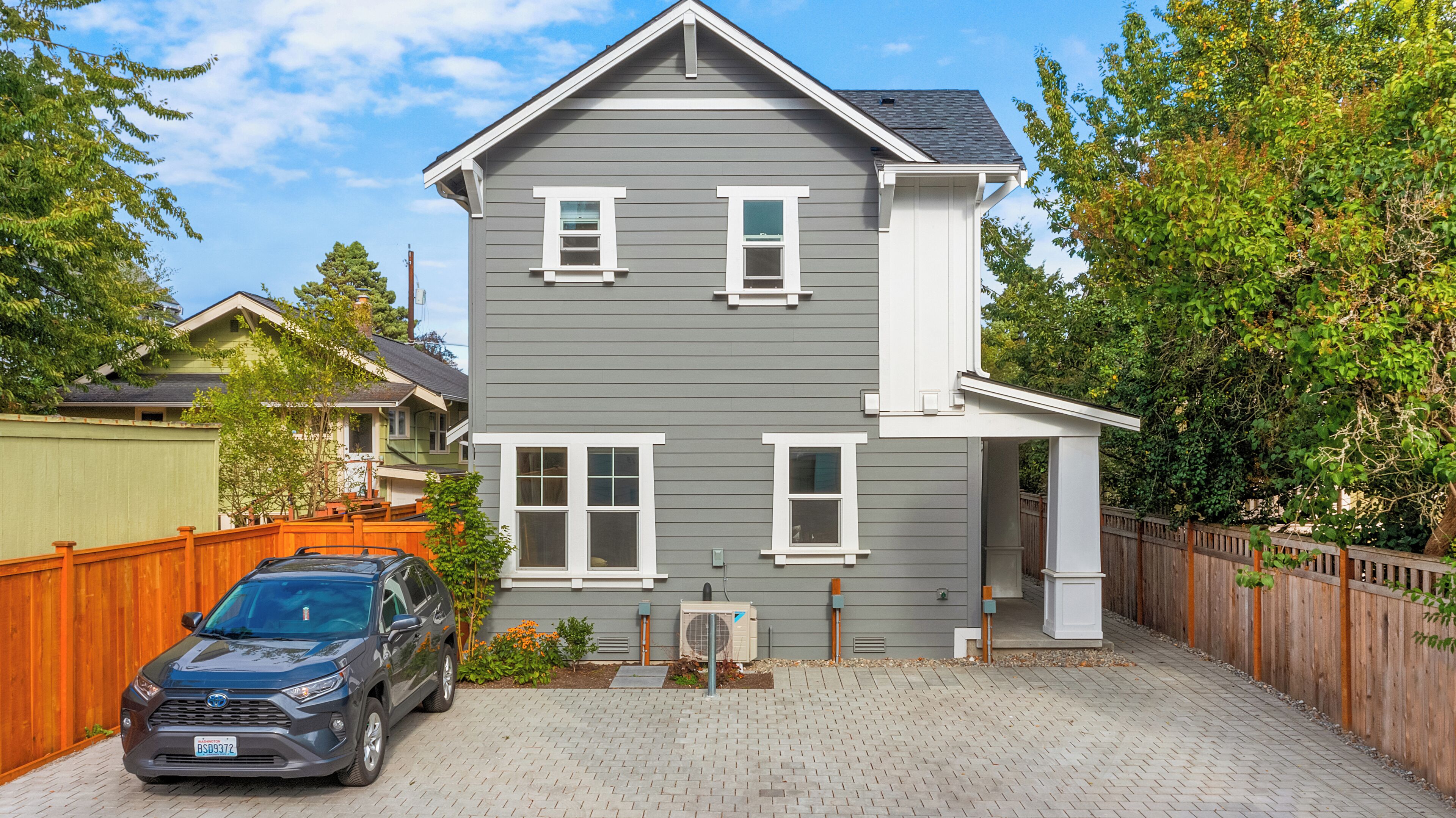 A two-story house with a grey exterior and white trim, a driveway, and a car parked in the driveway.