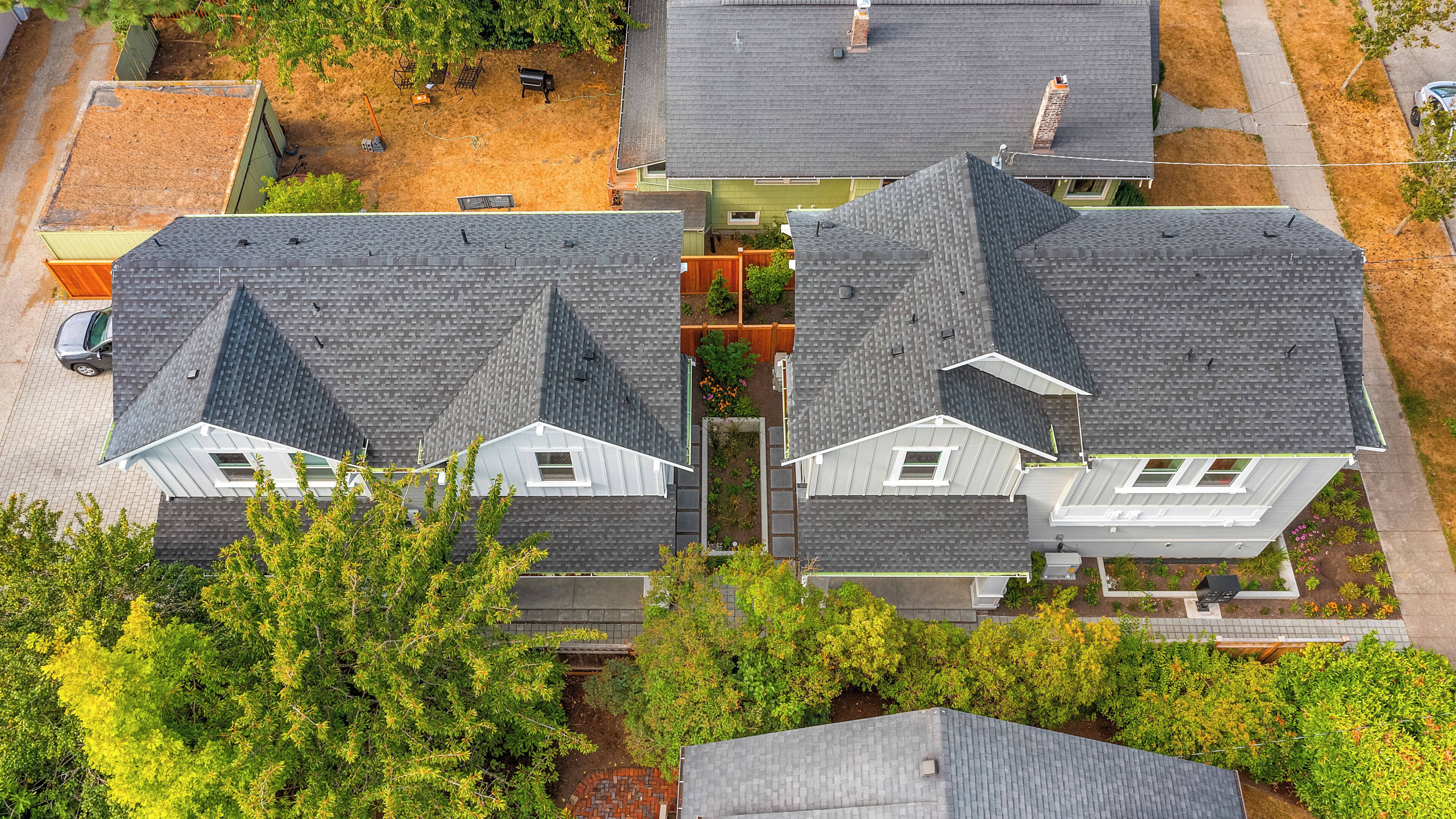 Zona residencial com duas casas, telhados cinzentos e detalhes brancos.