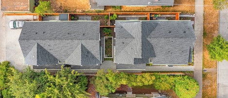 An aerial view of a residential area with two houses, a paved driveway, and surrounding greenery.