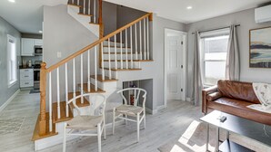 Ein modernes Interieur mit einer Holztreppe, weißen Stühlen, einem Ledersofa und einer Küchenzeile.