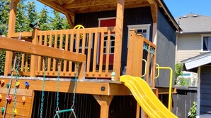 A wooden playhouse with a slide, climbing wall, and swing set. - Quiet Modern Stay Near SeaTac & Hospitals (Des Moines)