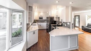 A modern kitchen with white cabinets, a large island, and a view through the sliding glass door. - Quiet Modern Stay Near SeaTac & Hospitals (Des Moines)