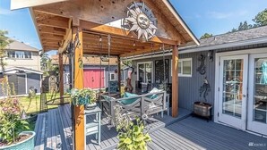 A covered outdoor patio with a wooden deck, a large decorative sun, and outdoor furniture. - Quiet Modern Stay Near SeaTac & Hospitals (Des Moines)