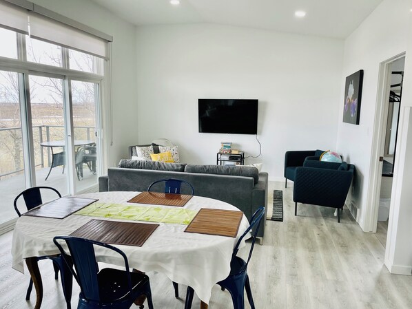 Una sala de estar moderna con una mesa de comedor, sillas, un sofá gris, un televisor y un sillón azul.